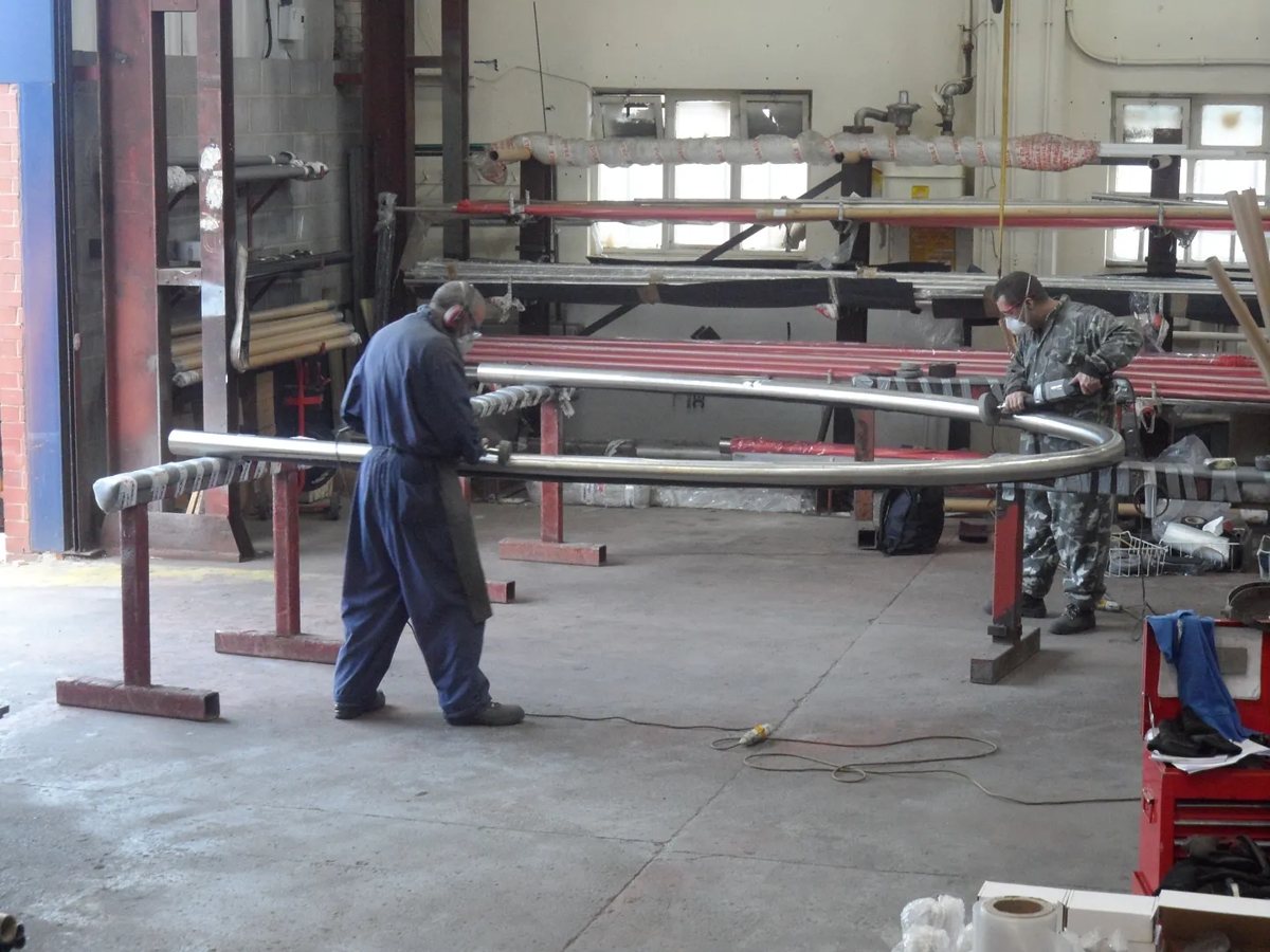 Two fabricators hand polishing a rolled stainless steel arch section to a satin finish in the workshop